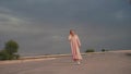 Beautiful model in dress walking towards camera, dark, cloudy sky on background