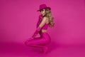 The beautiful model is wearing sexy pink shiny leggings, ankle boots, an elegant fuchsia top and a pink hat and is posing against Royalty Free Stock Photo
