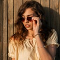 Beautiful model woman hipster put on a fashion sunglasses near vintage wooden wall at sunset Royalty Free Stock Photo