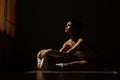 Beautiful modern ballet dancer with perfect body sits on the floor in the studio hall.