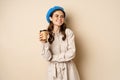 Beautiful modern girl posing with takeout cup of coffee, drinking from reusable cup from cafe and posing happy, beige
