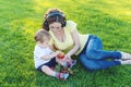 Beautiful modern mom playing in a green meadow with her cute baby son in a Sunny Park. Concept of the joy of motherhood Royalty Free Stock Photo