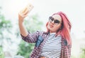 Beautiful modern smiling young female teenager with extraordinary hairstyle color in a checkered shirt and sunglasses taking