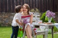 Beautiful mom, having coffee in a backyard, young cute child giving her present and flowers Royalty Free Stock Photo