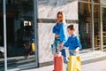 Beautiful mom and her cute little daughter are holding shopping bags, looking at camera and smiling while standing outdoors. Royalty Free Stock Photo