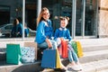 Beautiful mom and her cute little daughter are holding shopping bags, looking at camera and smiling while standing outdoors. Royalty Free Stock Photo