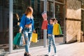 Beautiful mom and her cute little daughter are holding shopping bags, looking at camera and smiling while standing outdoors. Royalty Free Stock Photo