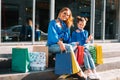 Beautiful mom and her cute little daughter are holding shopping bags, looking at camera and smiling while standing outdoors. Royalty Free Stock Photo