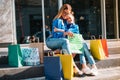 Beautiful mom and her cute little daughter are holding shopping bags, looking at camera and smiling while standing outdoors. Royalty Free Stock Photo