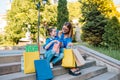 Beautiful mom and her cute little daughter are holding shopping bags, looking at camera and smiling while standing outdoors. Royalty Free Stock Photo