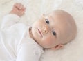 Beautiful 6 Month Baby Boy Dressed in White & Lying on Fluffy White Blanket Looking at Camera. Smiling & Happy