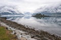 Beautiful morning landscape on fjord with creeping clouds. Rocky island with trees and wonderful reflection in the water, Norway