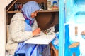 A beautiful Moroccan girl, a Muslim, street artist paints a picture with a brush in a small workshop