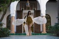 Beautiful Moroccan Girl walking and Waving her white mantle in Rich interior of Picturesque Dar Si Said Riyad in