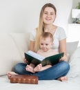 Beautiful young mother with baby boy sitting on bed and holding big old book Royalty Free Stock Photo