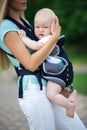 Beautiful mother with baby boy in sling walking in green park Royalty Free Stock Photo