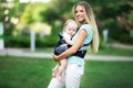 Beautiful mother with baby boy in sling walking in green park Royalty Free Stock Photo