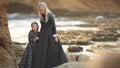 Beautiful mother blonde in a long gray dress with her little daughter in a dress on the beach