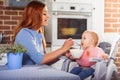 Beautiful mother in blue dress feeding with spoon her cute baby girl witch sits in high chair. Royalty Free Stock Photo