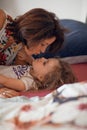 Beautiful mother cuddles with her daughter in bed, giggling and laughing and kissing