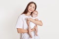 Beautiful mother dresses in casual t shirt, holding baby in bodysuit with nipple isolated over white background, looking directly Royalty Free Stock Photo