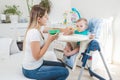 Beautiful mother feeding her baby boy in highchair with porridge Royalty Free Stock Photo
