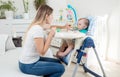 Beautiful mother feeding her baby boy in highchair Royalty Free Stock Photo