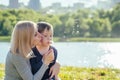 Beautiful mother and her cute baby son blowing blow away a dandelion balloon in the park on a background of green grass Royalty Free Stock Photo