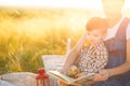 Beautiful mother and her cute son reading a book on a picnic on the sunset background. Happy family and education concept