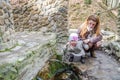 Beautiful mother with her daughter Baby drink water from the holy spring that flows from the rock among the vegetation Royalty Free Stock Photo