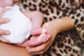 Beautiful mother in leopard robe breastfeed her newborn baby in white bodysuit holding feet in hand. Selective focus. Royalty Free Stock Photo