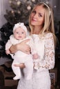 Beautiful mother posing with her cute little baby girl beside Christmas tree Royalty Free Stock Photo