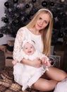 Beautiful mother posing with her cute little baby girl beside Christmas tree Royalty Free Stock Photo