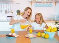 Beautiful mother pours orange juice to her daughter with a smile. concept of happy family. dressed in white t-shirts