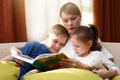 Beautiful mother is reading a book to her young children. Sister Royalty Free Stock Photo