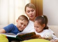 Beautiful mother is reading a book to her young children. Sister and brother is listening to a story. Royalty Free Stock Photo