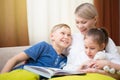 Beautiful mother is reading a book to her young children. Sister and brother is listening to a story.