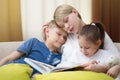 Beautiful mother is reading a book to her young children. Sister and brother is listening to a story.