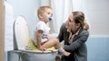 Beautiful young mother sitting next to her toddler boy on toilet