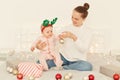 Beautiful mother sitting on white bed and holding baby in her arms, smiling, celebrating New Year`s holidays, playing with Royalty Free Stock Photo