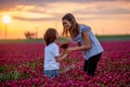 Beautiful mother and son in crimson clover field, mom getting bouquet of wild flowers gathered from her child for Mothers day