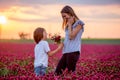 Beautiful mother and son in crimson clover field, mom getting bouquet of wild flowers gathered from her child for Mothers day