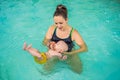 Beautiful mother teaching cute baby girl how to swim in a swimming pool. Child having fun in water with mom Royalty Free Stock Photo