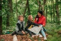 Beautiful mother with two kids are having break in the forest, using a map and planning a hiking adventure Royalty Free Stock Photo