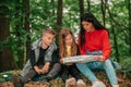 Beautiful mother with two kids are sitting in forest, using a map and planning a hiking adventure Royalty Free Stock Photo