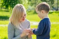 Beautiful mother wipes hands with napkins of cute baby son in the park on a background of green grass and trees