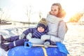 Beautiful mother woman with baby boy 3 years old, sitting inflatable tubing, rolling down from hill, having rest, winter Royalty Free Stock Photo