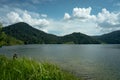 Beautiful mountain lake landscape, cloudy blue sky and green grass field. Man relaxing alone at lake in front of the mountain, Mal Royalty Free Stock Photo