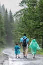 Beautiful mountain landscape. Father, son and daughter are walking on a wet road after a heavy rain in raincoats. The boy is Royalty Free Stock Photo