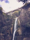 Beautiful mountain waterfall with a falling stream of water flowing from under a bridge on a cliff overgrown with trees and plants Royalty Free Stock Photo